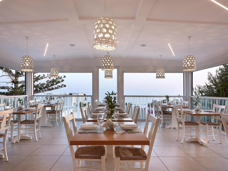 Restaurant ouvert avec vue sur la mer, tables dressées et éclairage moderne.
