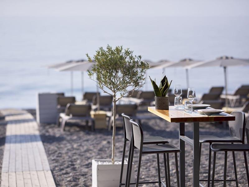 Table et chaises modernes sur la plage avec des chaises longues et des parasols en arrière-plan.