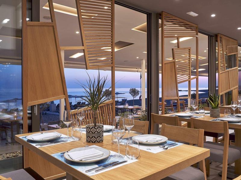 Restaurant moderne avec meubles en bois et vue sur la mer au coucher du soleil.