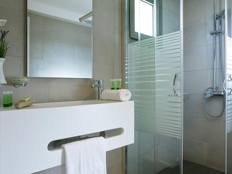 Salle de bain moderne avec douche, lavabo et serviettes dans une chambre d'hôtel.