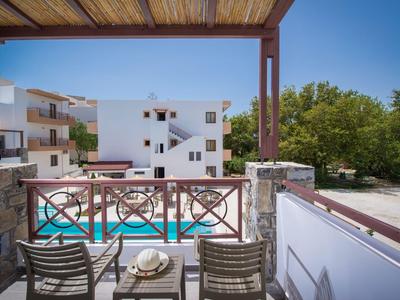 Vista da un balcone con sedie su un hotel con piscina e edifici bianchi sotto un cielo sereno.