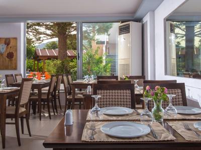 Hell eingerichteter Speiseraum mit großen Fenstern, gedeckten Tischen und Blick ins Grüne.