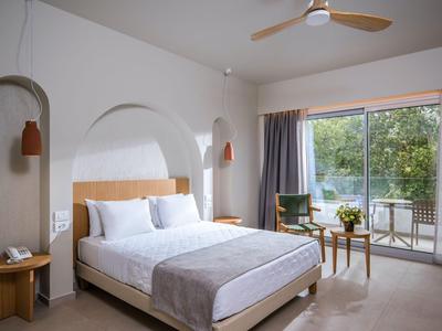 Camera d'hotel moderna con letto matrimoniale, area salotto e grande porta scorrevole verso terrazza con vista sul verde.