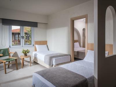 Modernes, minimalistisches Schlafzimmer mit zwei Betten, Stühlen, Tisch und Zugang zu einem angrenzenden Raum.