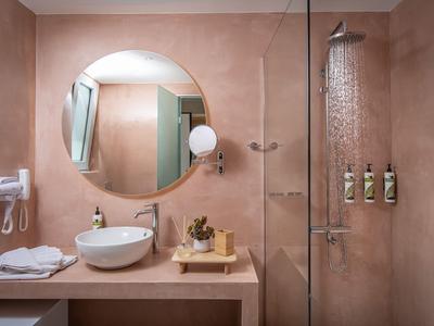 Nowoczesna łazienka hotelowa z okrągłym lustrem, umywalką i prysznicem w ciepłych piaskowych tonach.