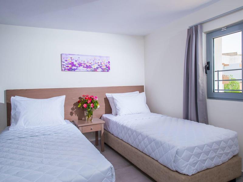 Helles Schlafzimmer mit zwei Einzelbetten, Nachttisch und Fenster mit grauen Vorhängen.