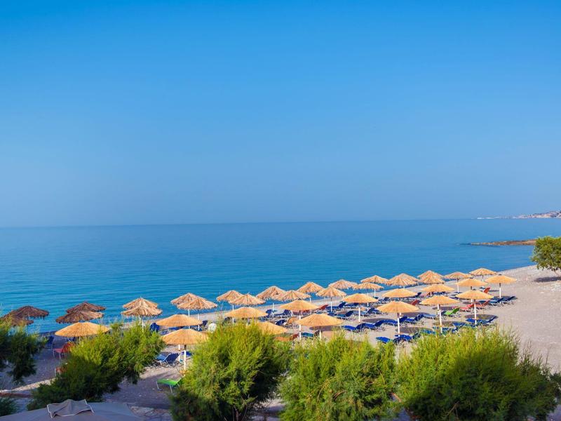 Strand mit Sand, vielen gelben Sonnenschirmen, blauem Meer und wolkenlosem Himmel.