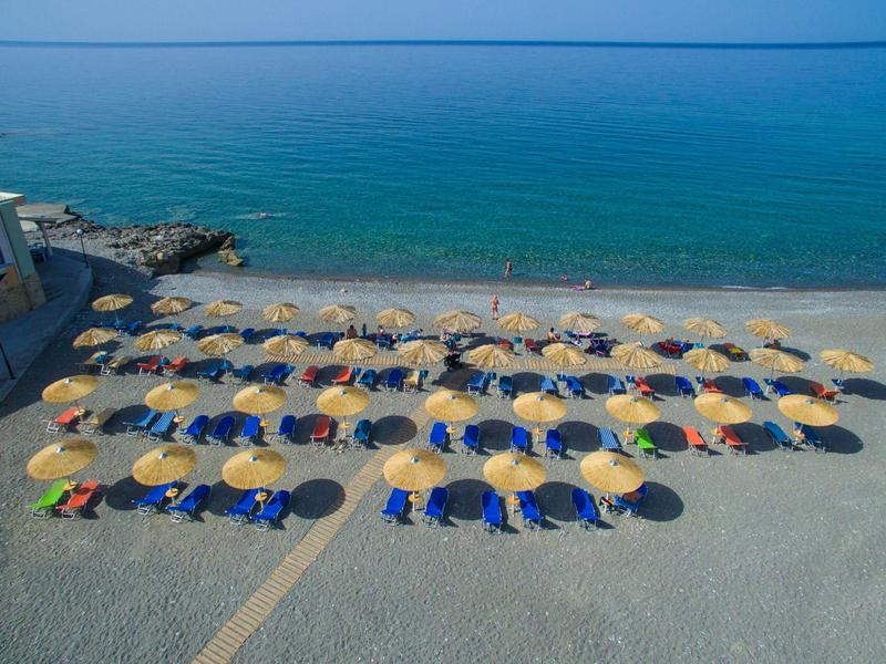 Strand mit Reihen gelber Sonnenschirme und blauen Liegestühlen am ruhigen blauen Meer.