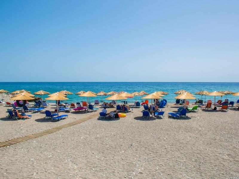 Strand mit Reihen von gelben Sonnenschirmen, Liegestühlen und blauem Meer unter klarem Himmel.