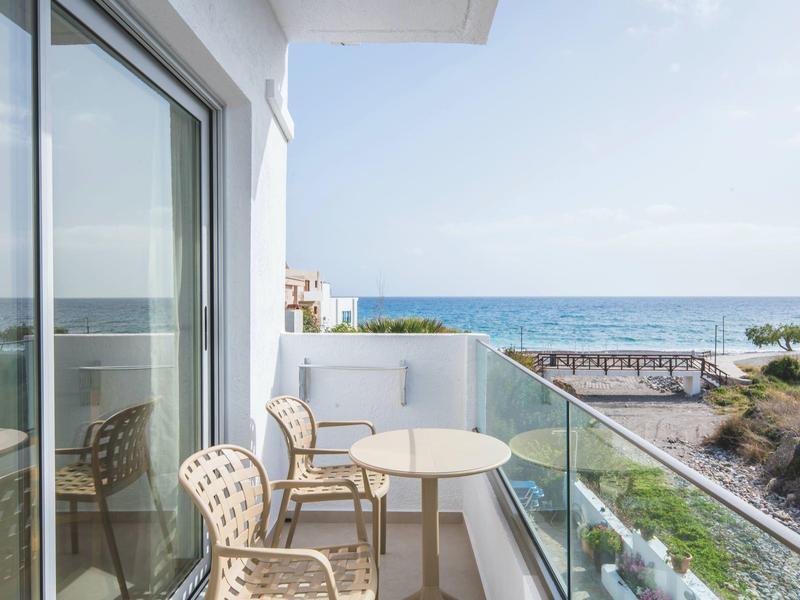 Balkon mit Glasgeländer, zwei Stühlen und kleinem Tisch, Meeresblick bei klarem Himmel.