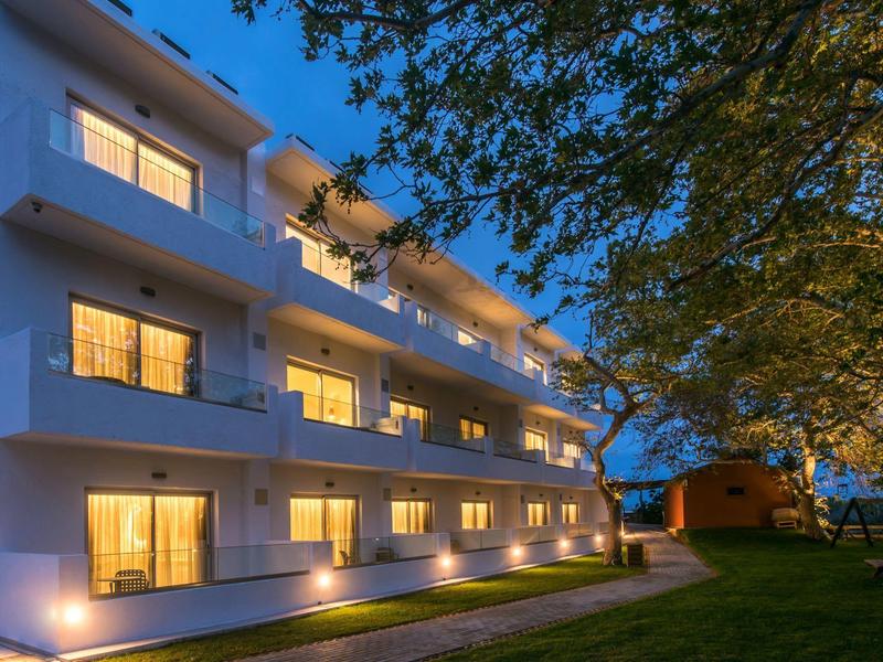 Modernes dreistöckiges Wohnhaus mit beleuchteten Fenstern im Abendlicht und grünem Garten.