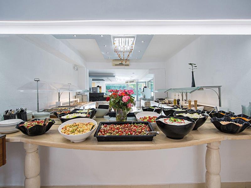 Buffet mit verschiedenen Salaten in schwarzen Schalen auf einem hellen Holztisch in hellem Raum.