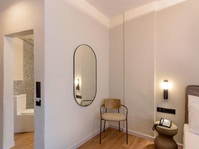 Nowoczesny pokój hotelowy z jasną drewnianą podłogą, krzesłem, owalnym lustrem i lampką nocną.