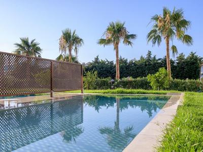 Czysty basen obok zielonego trawnika i palm pod niebieskim niebem.