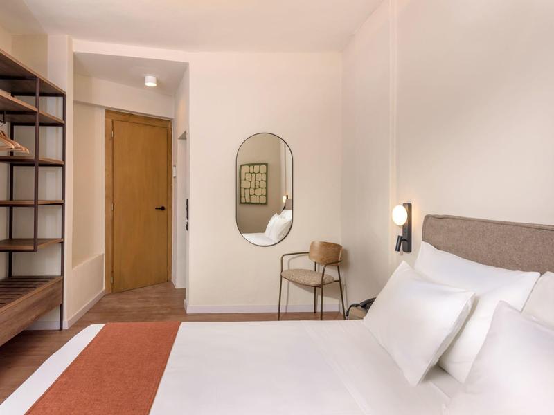 Nowoczesny pokój hotelowy z wygodnym łóżkiem, krzesłem, lustrem ściennym i otwartą półką.