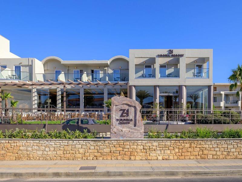 Nowoczesny budynek hotelowy z tarasem i leżakami pod jasnym, niebieskim niebem.