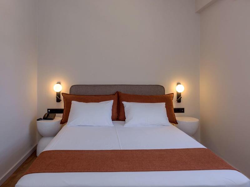 Prosto urządzone dwuosobowe pokoje z łóżkiem, białymi ścianami i przytulnym oświetleniem.