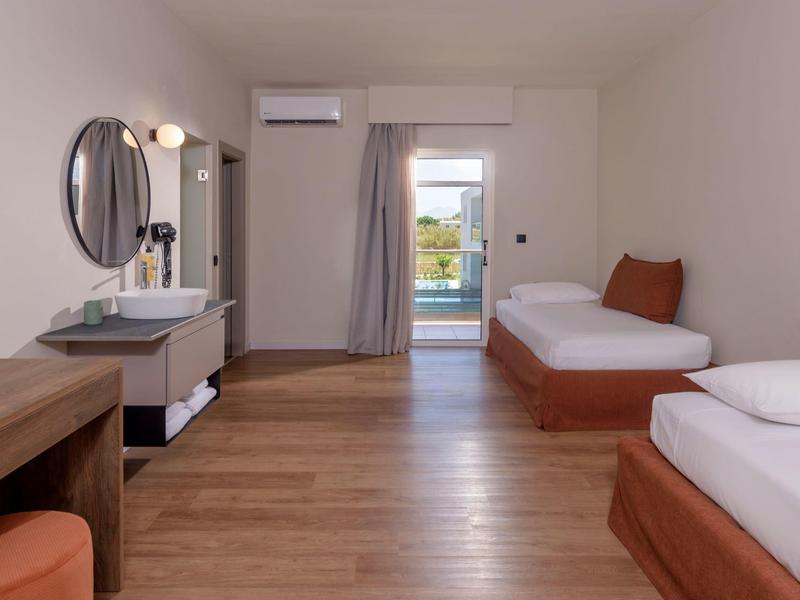 Prosty pokój hotelowy z dwoma łóżkami pojedynczymi, drewnianą podłogą i umywalką.