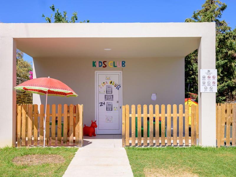 Mały domek klubu dziecięcego z płotem, czerwoną parasolką i trawą z przodu