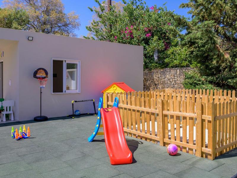 Plac zabaw dla dzieci z kolorową zjeżdżalnią obok małego budynku i ogrodzonego piaskownicy.