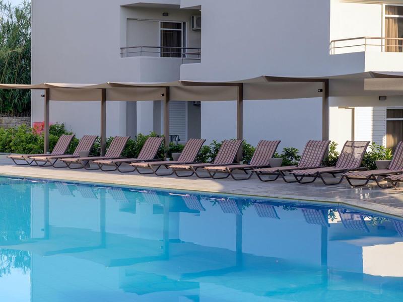 Pusty basen na zewnątrz z leżakami i parasolami przed nowoczesnym budynkiem.