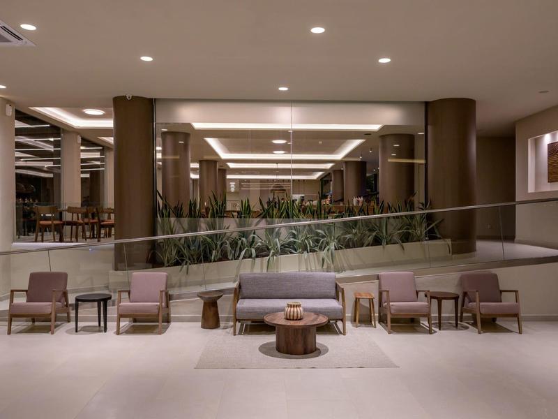 Nowoczesna lobby hotelowa z kilkoma krzesłami i stolikami przed zieloną przegrodą.