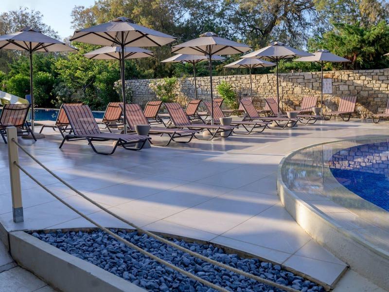 Rząd leżaków z parasolami obok basenu w hotelowym ogrodzie.