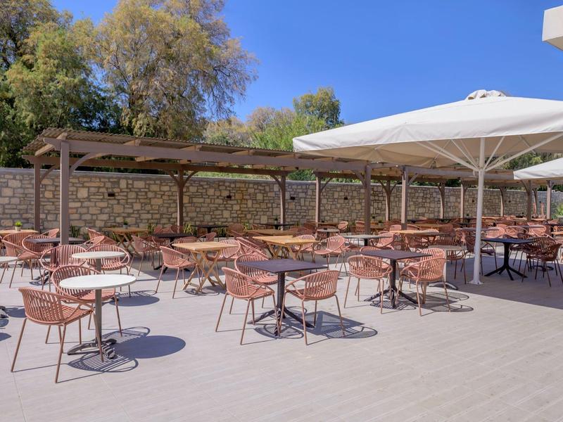 Pusta zewnętrzna terasa z stołami, krzesłami i dużymi parasolami w słoneczny dzień.