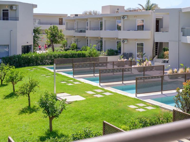 Nowoczesny kompleks hotelowy z basenami, zielonym trawnikiem i małymi drzewami.