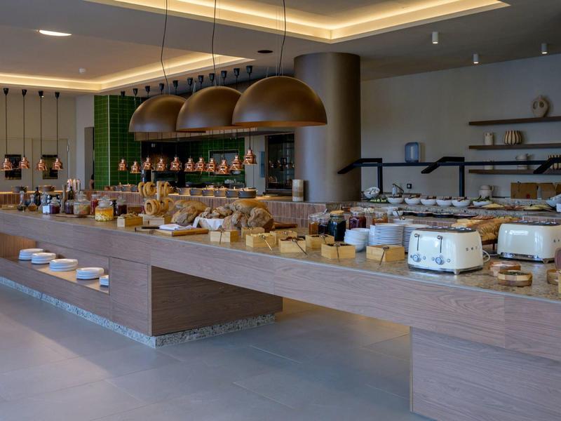 Nowoczesna kuchnia hotelowa z bufetem i różnymi rodzajami pieczywa pod wiszącymi lampami.