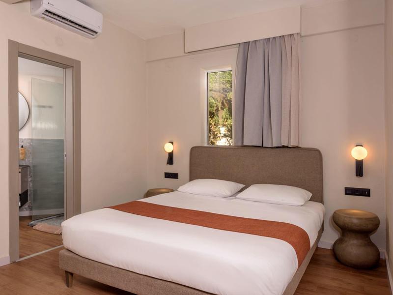 Przytulny pokój hotelowy z łóżkiem podwójnym, dwoma stolikami nocnymi i widokiem na łazienkę.