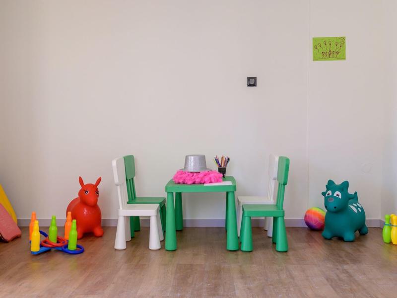 Pokój dziecięcy z zielono-białym stołem i krzesłami, kolorowymi zabawkami i figurkami na drewnianej podłodze.