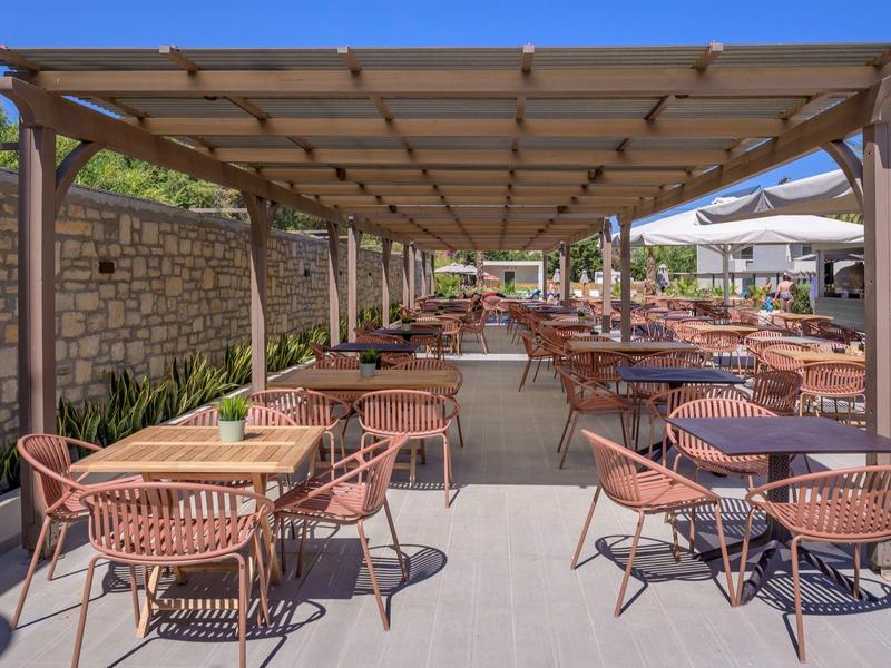 Duży zadaszony taras na zewnątrz z wiklinowymi krzesłami i stołami obok kamiennego muru i roślin.