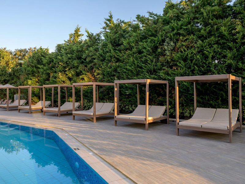 Rząd nowoczesnych leżaków z daszkami obok basenu i zielonych drzew.