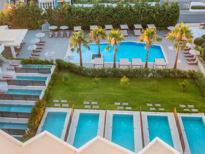 Widok na basen hotelowy z leżakami, palmami i prywatnymi basenami poniżej.