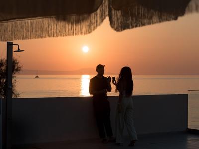 Twee personen staan op een hotelterras bij zonsondergang met uitzicht op zee.