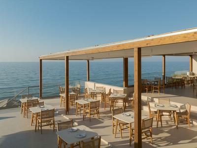 Open restaurantgebied met houten meubels en uitzicht op zee bij zonnig weer.