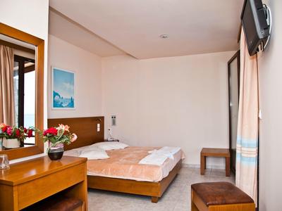 Helles Schlafzimmer mit Doppelbett, Holzmöbeln, Blumen und einem Fernseher an der Wand.