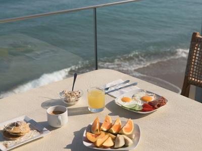 Ontbijt met sinaasappelsap, koffie en fruit op een tafel met uitzicht op de zee.