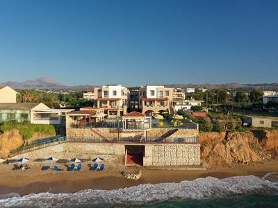 Strand mit blau-weißen Liegestühlen und Häusern auf felsigem Hügel bei klarem Himmel.