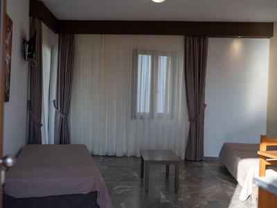 Kleines Zimmer mit zwei Betten, Vorhängen an Fenster und Marmorboden. Einfaches, sparsames Mobiliar.