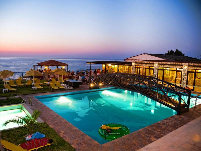 Beleuchteter Pool mit Sonnenliegen und Strandblick bei Sonnenuntergang, gemütliche Terrasse.