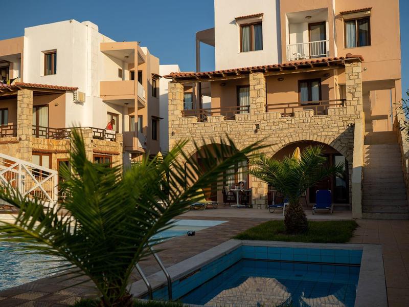 Mehrstöckiges Gebäude mit Steinmauer, Holzbalkonen, Pool und grünen Palmen unter blauem Himmel.