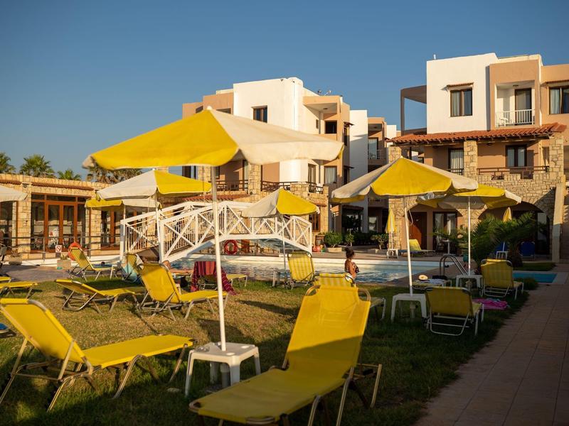 Sonnige Terrasse mit gelben Sonnenschirmen und Liegestühlen vor mehrstöckigen Gebäuden.