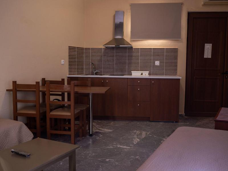 Kleine Küche mit dunklen Schränken, Fliesenspiegel, Esstisch mit Holzstühlen und grauem Boden.