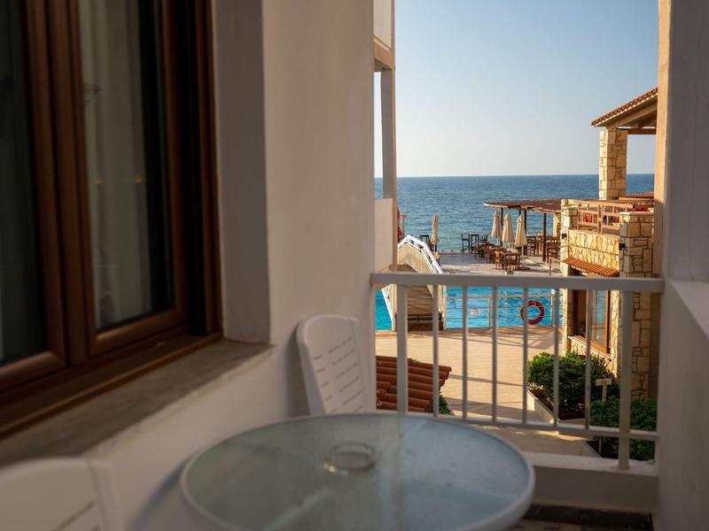 Blick von Balkon mit weißem Tisch und Stuhl auf Pool, Meer und blauen Himmel im Hintergrund.
