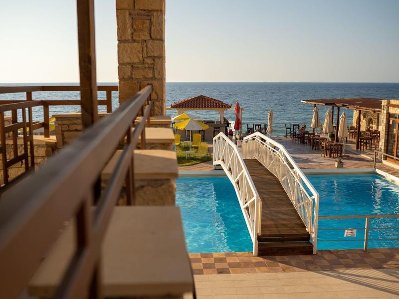 Poolbereich mit kleinem weißen Bogen über dem Wasser und Blick auf das Meer bei Sonnenuntergang.
