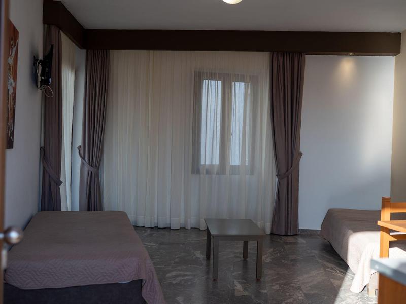 Kleines Zimmer mit zwei Betten, Vorhängen an Fenster und Marmorboden. Einfaches, sparsames Mobiliar.