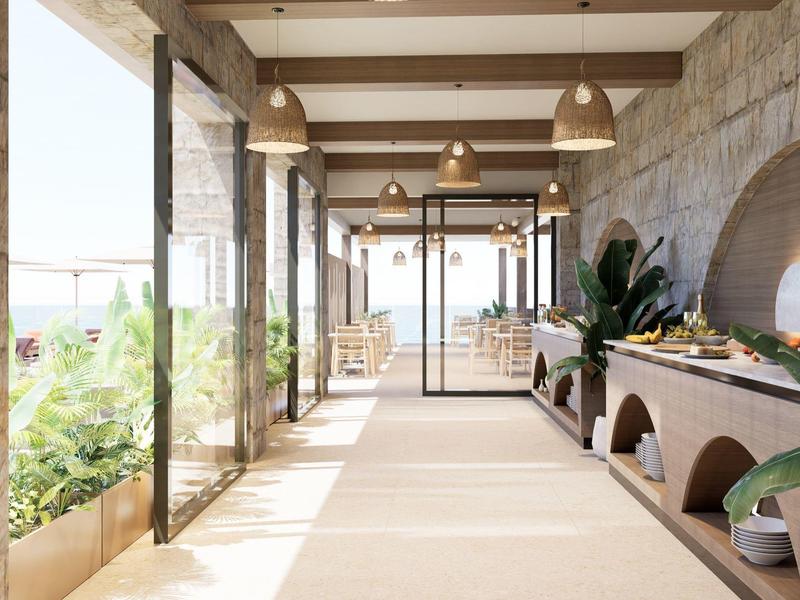 Heller Hotelflur mit Natursteinwänden, Pflanzen und großen Fenstern mit Meerblick.