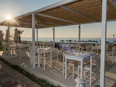 Area pranzo aperta con tavoli e sedie bianchi al tramonto sulla spiaggia.